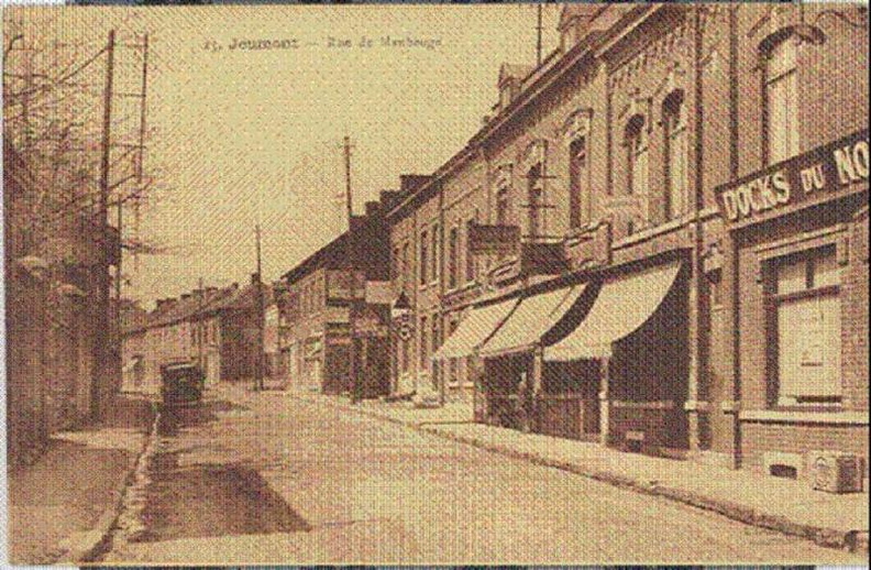 Sur la droite, on aperçoit « les Docks du Nord » ( épicerie, alimentation générale).
Le premier auvent était la papeterie « Mathieu »; le deuxième, un coiffeur,sous l’enseigne « Au palais des parfums »; le troisième la boucherie moderne tenue par Monsieur Depret.
Cette boucherie deviendra plus tard la « boucherie chevaline ».
Juste après était installée la banque du Crédit du Nord, suivie d’une herboristerie tenue par Madame Delos qui cédera sa place à un marchand de chaussures.
Ensuite, une boutique de vélos, motos et aussi de téléviseur ! aujourd’hui remplacée par le coiffeur « chez Claudine ».
Le mur de gauche était l’enceinte de l’agence en douanes Auguste Marchal, famille très importante de Jeumont.
Photo prise vers 1950. Blum_001.jpg